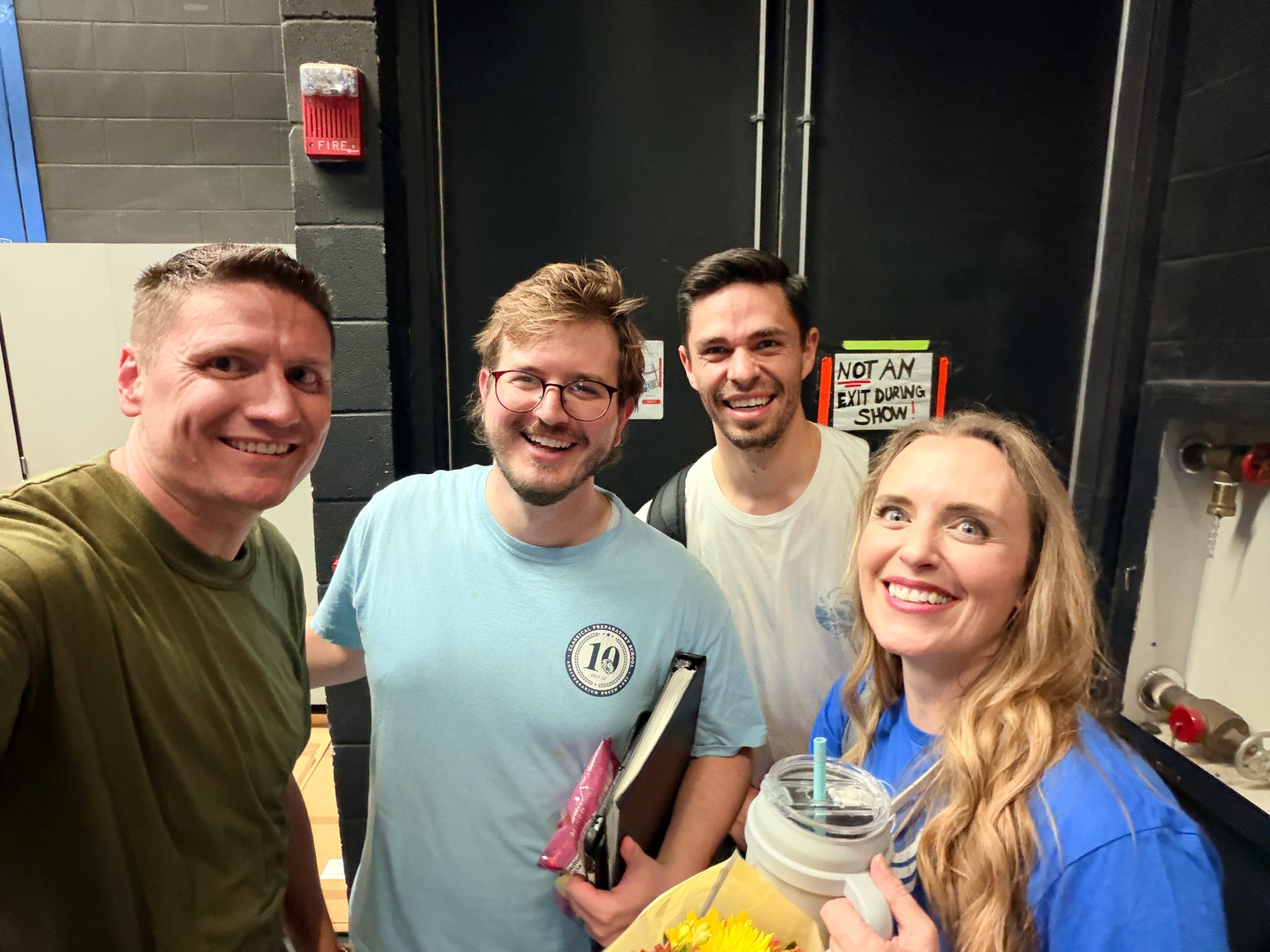 Four volunteers smiling together in a backstage hallway